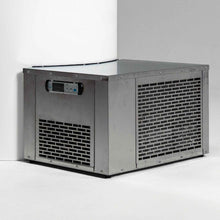 A metal ice maker machine with a digital control panel, positioned in a corner against a white wall.