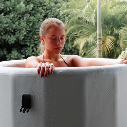 A woman with her eyes closed relaxes in a hot tub, surrounded by lush greenery. Water droplets glisten on her skin as she leans back, enjoying the serene atmosphere.