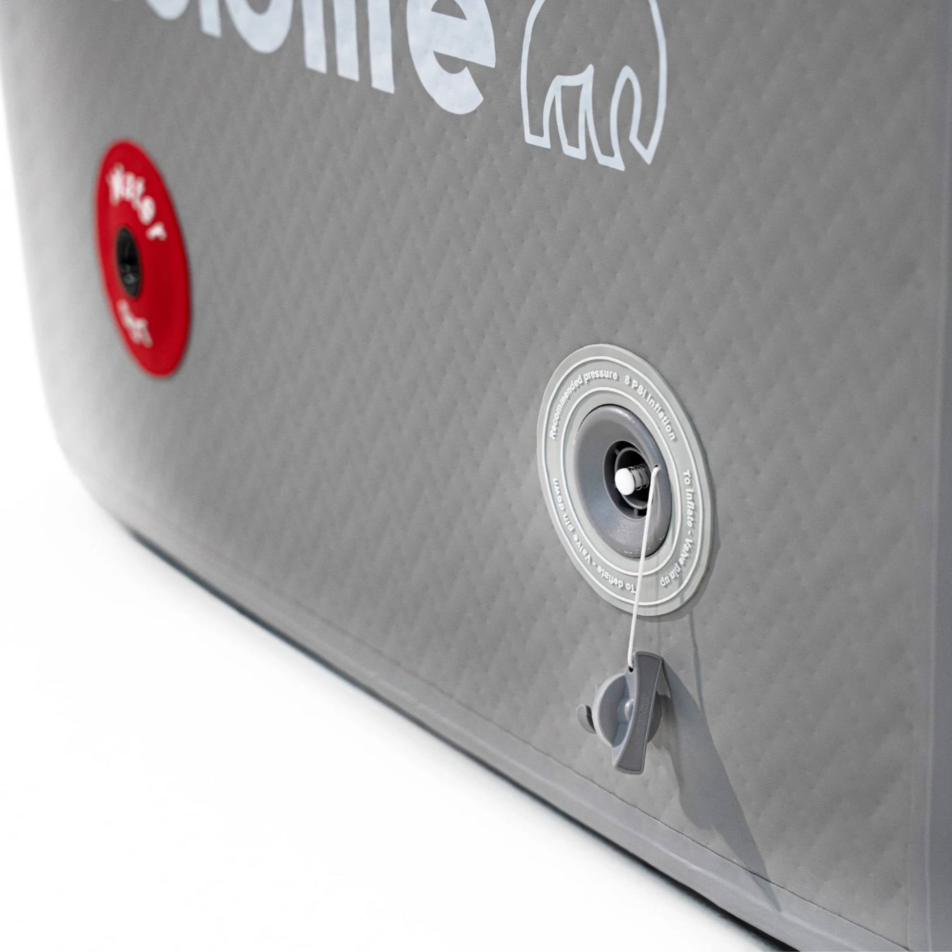 Close-up of a gray inflatable product featuring a logo and two valves, one red labeled Inflate and the other gray with instructions for pressure regulation.