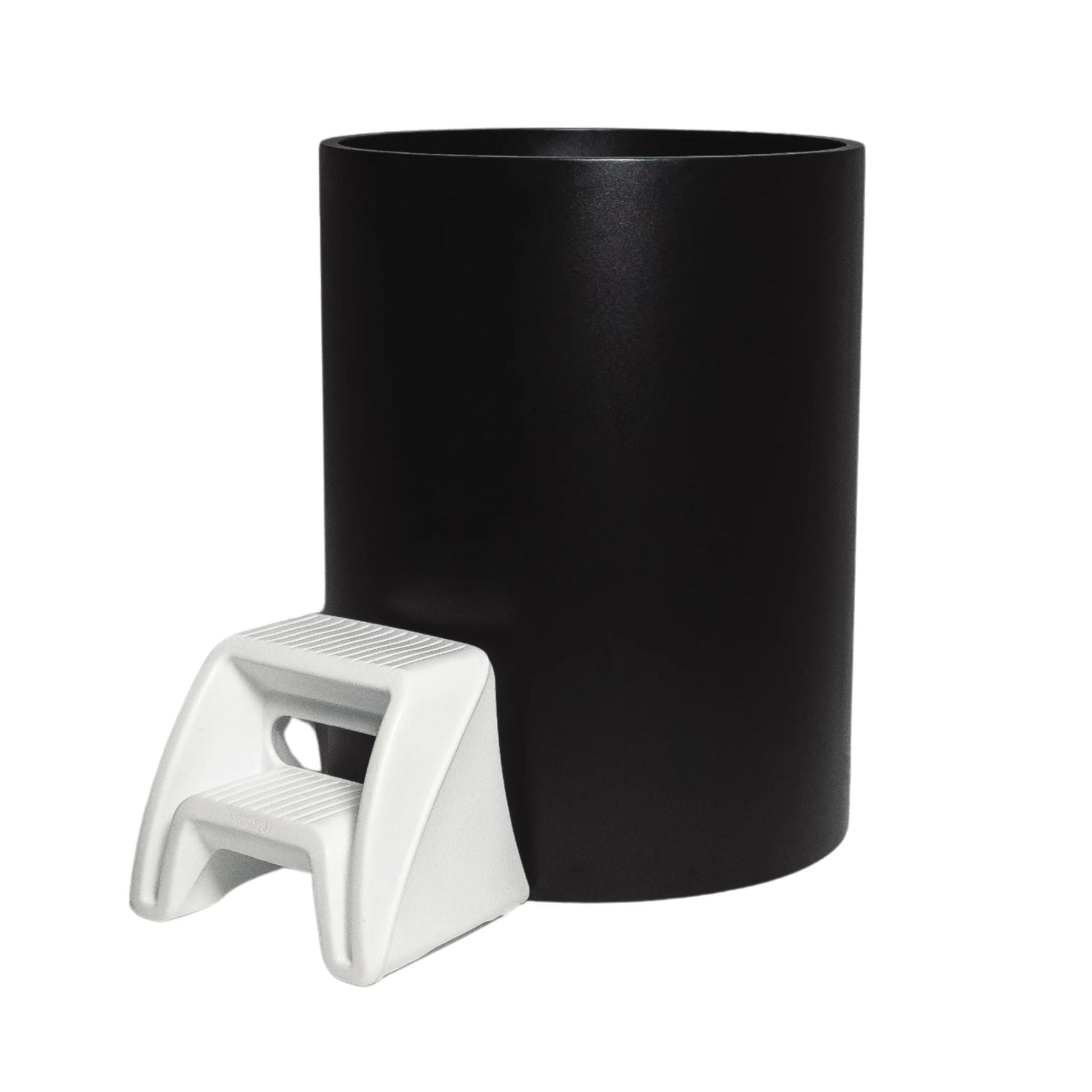 A black cylindrical container with a small white step stool positioned next to it.